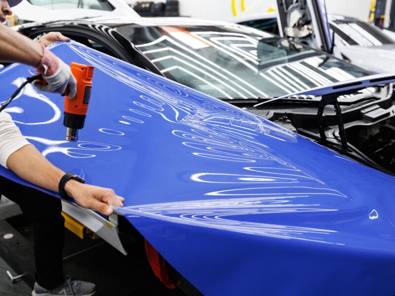 Technician using heat gun to fit paint protection film on car hood
