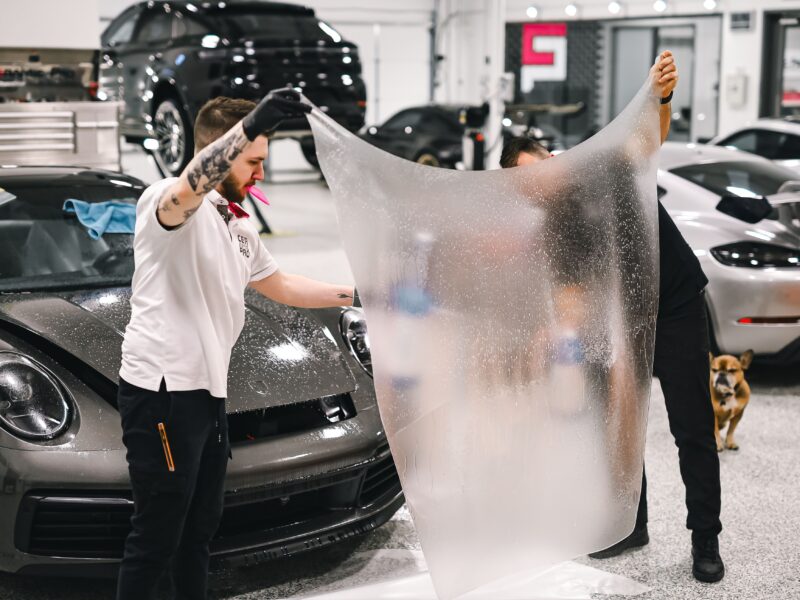 Technicians holding paint protection film sheet during car installation